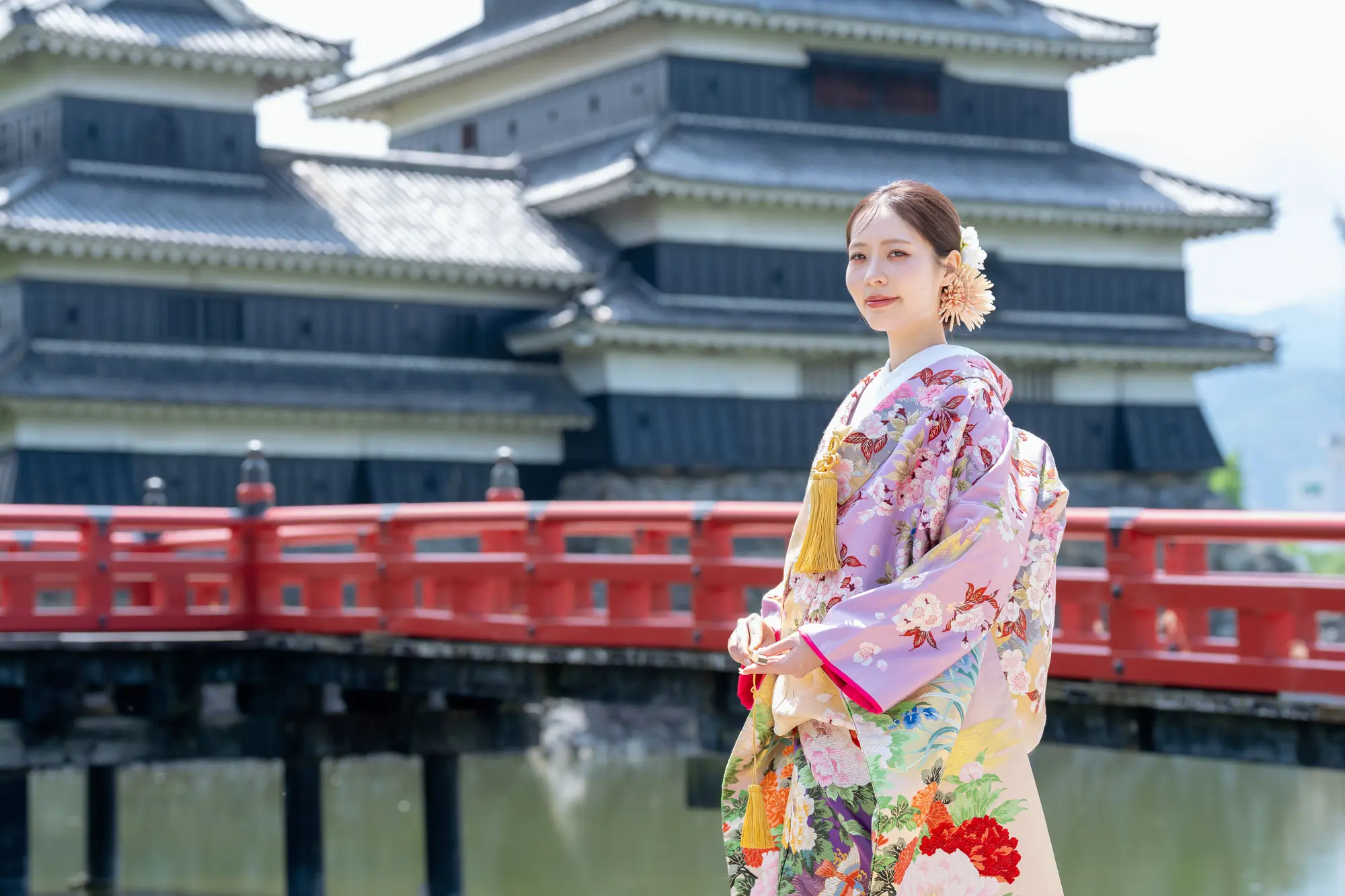松本城の赤い埋橋を背景に立つ、淡い色打掛の花嫁