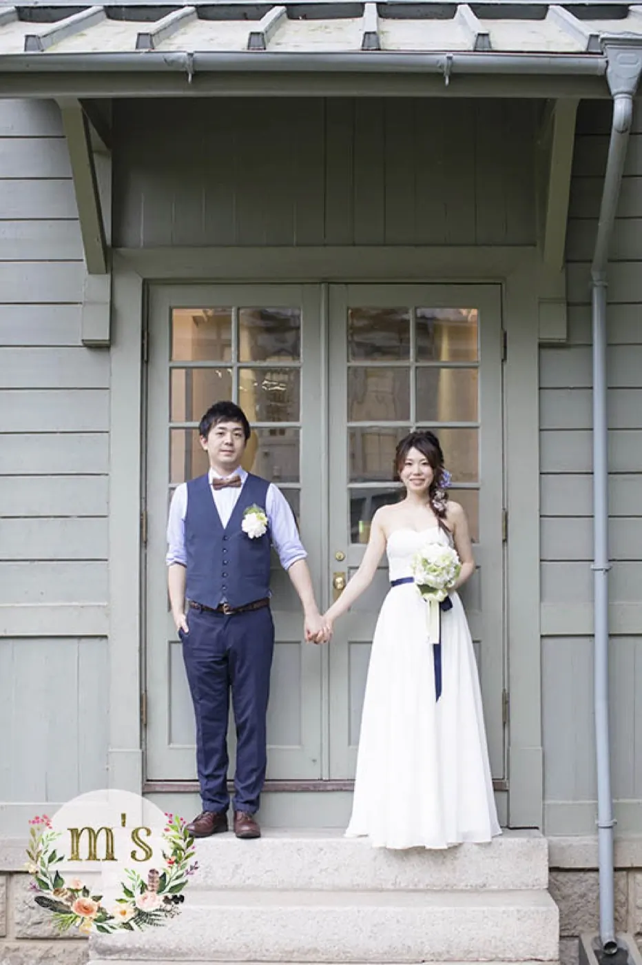 洋館の扉の前に並ぶ、ウェディングドレスとタキシードの新郎新婦