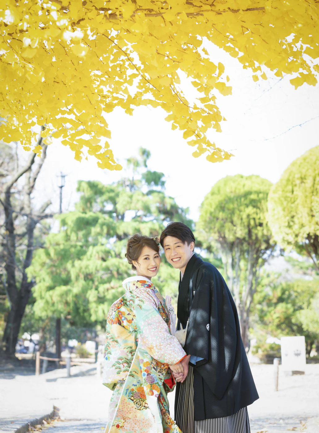 黄色く色づいた銀杏の下で振り返る、水色の色打掛の花嫁と黒紋付袴の花婿