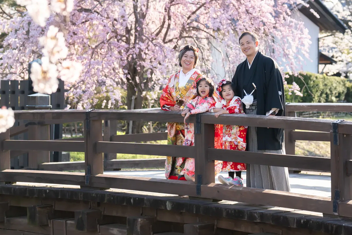 松本城の外堀にかかる橋の上で、満開の桜を背に並ぶ和装の家族