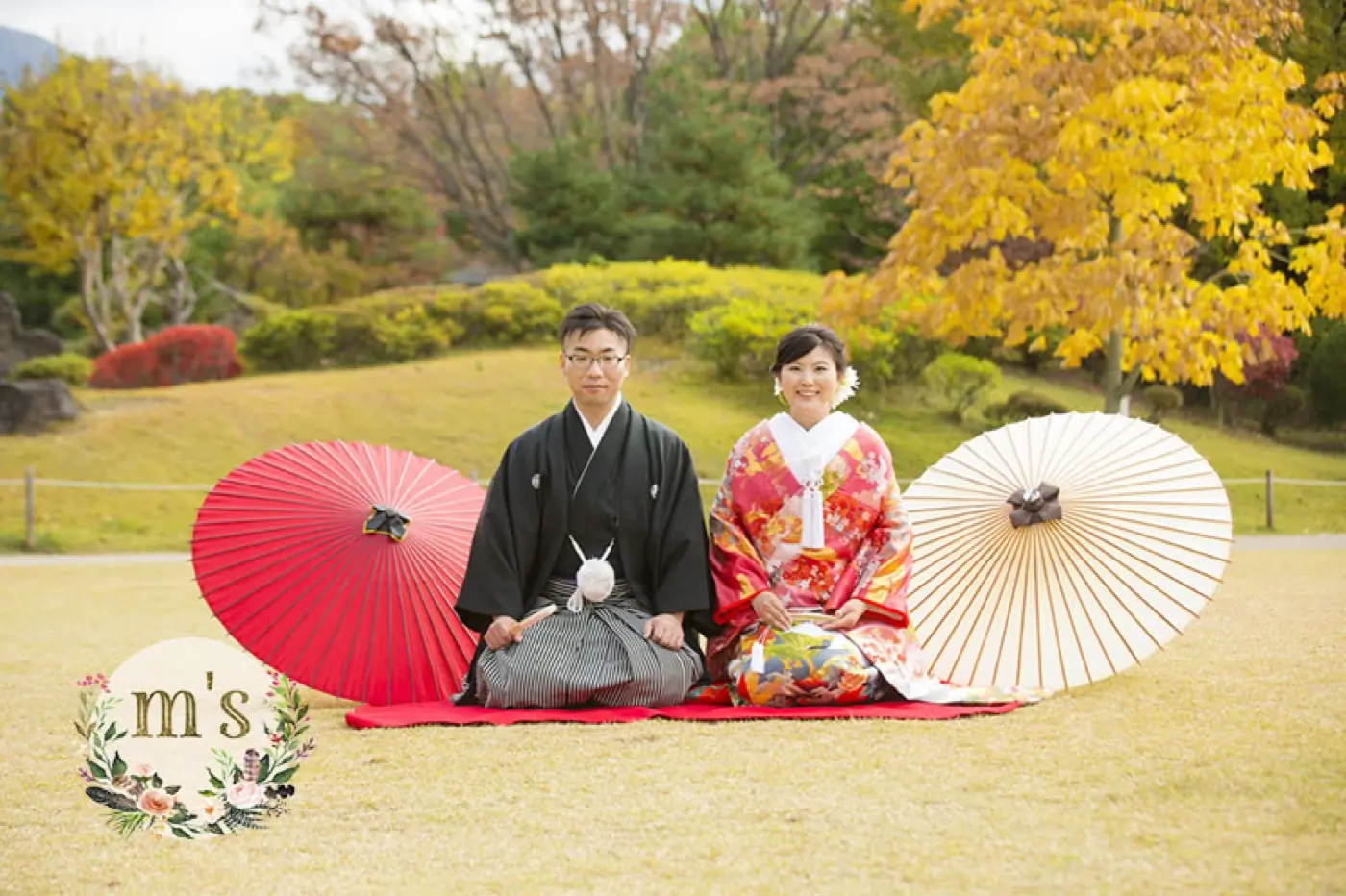 黄葉した銀杏の下、赤い和傘を並べて座る和装の新郎新婦
