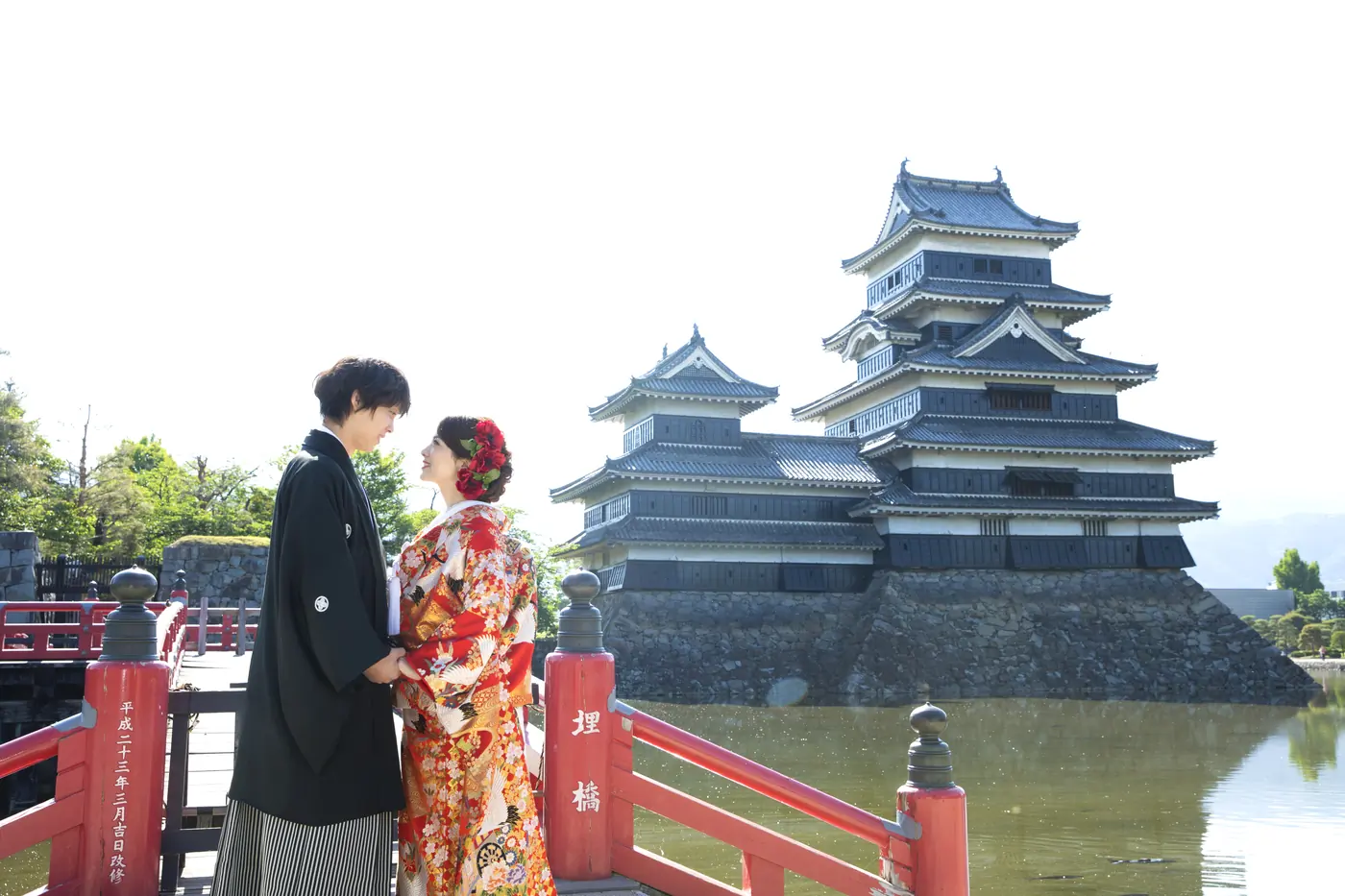 松本城の赤い埋橋の上で向かい合う、色打掛の花嫁と黒紋付袴の花婿