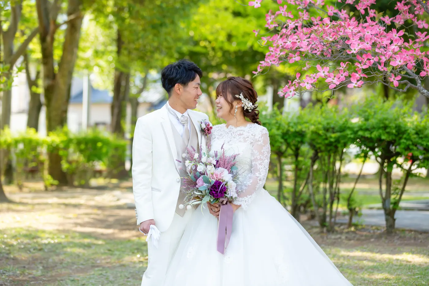 桃の花が咲く公園で、ブーケを持つウェディングドレスの花嫁と白いタキシードの花婿