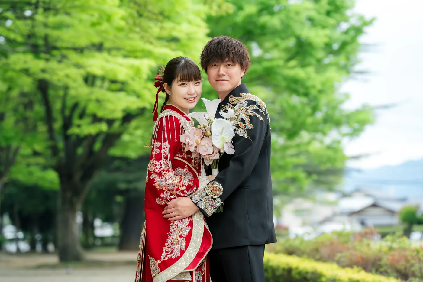新緑の並木で寄り添う、赤い色打掛の花嫁と黒紋付袴の花婿