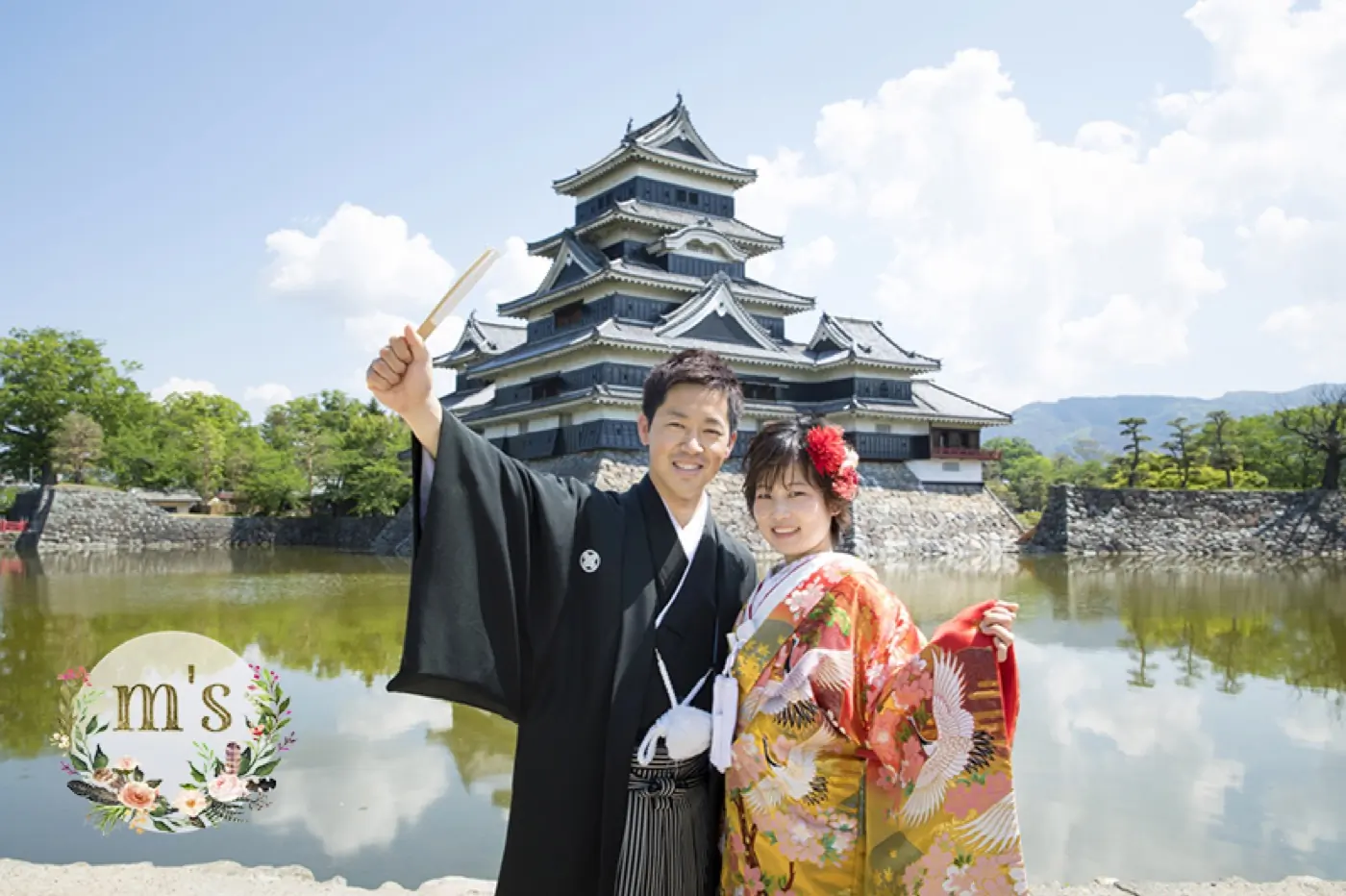 松本城の天守を背景に、色打掛の花嫁と黒紋付袴の花婿が手をつなぐ和装前撮り