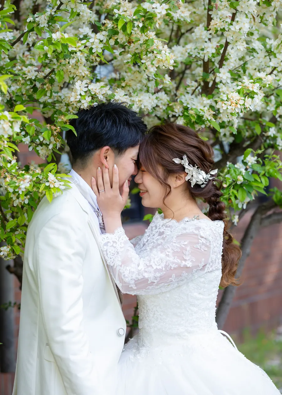 花の下で顔を寄せ合う、ウェディングドレスの花嫁とタキシードの花婿