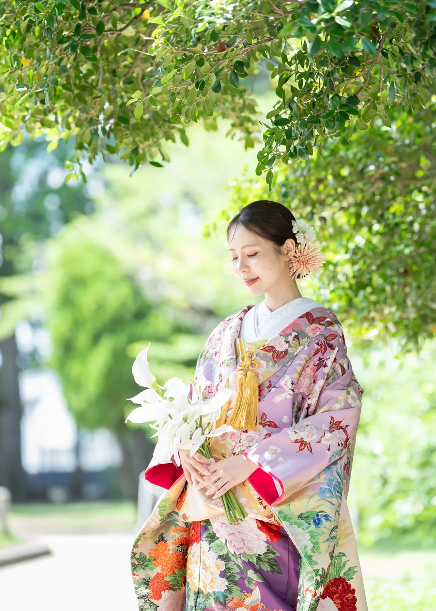 百合の和装ブーケを持ち、木漏れ日の下に立つ色打掛の花嫁