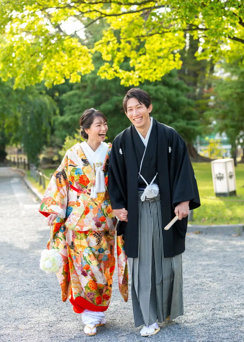 色打掛と黒紋付袴で並んで歩きながら笑い合う、和装前撮りの新郎新婦