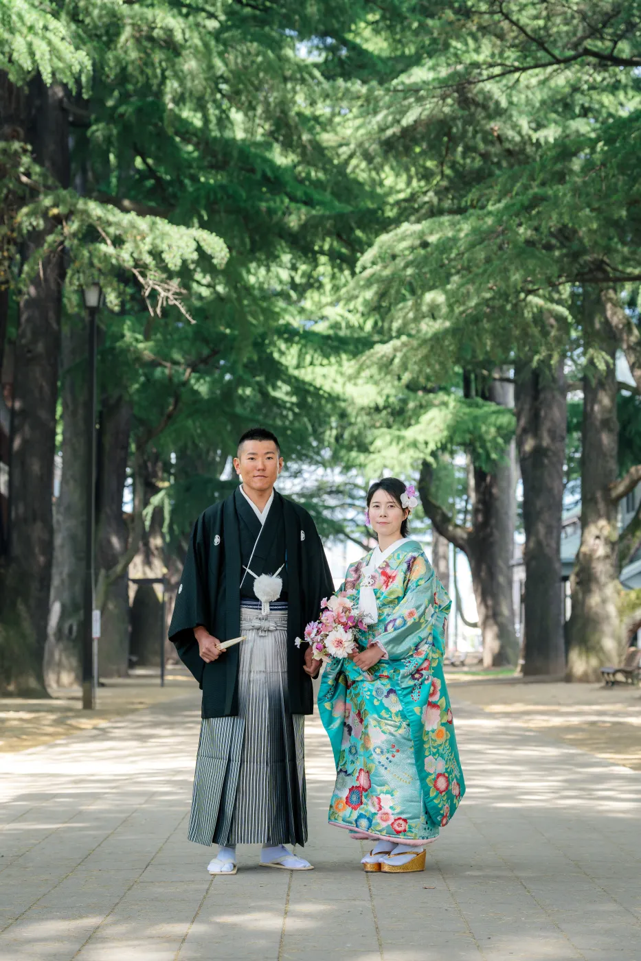 ヒマラヤ杉の並木道に並んで立つ、水色の色打掛の花嫁と黒紋付袴の花婿