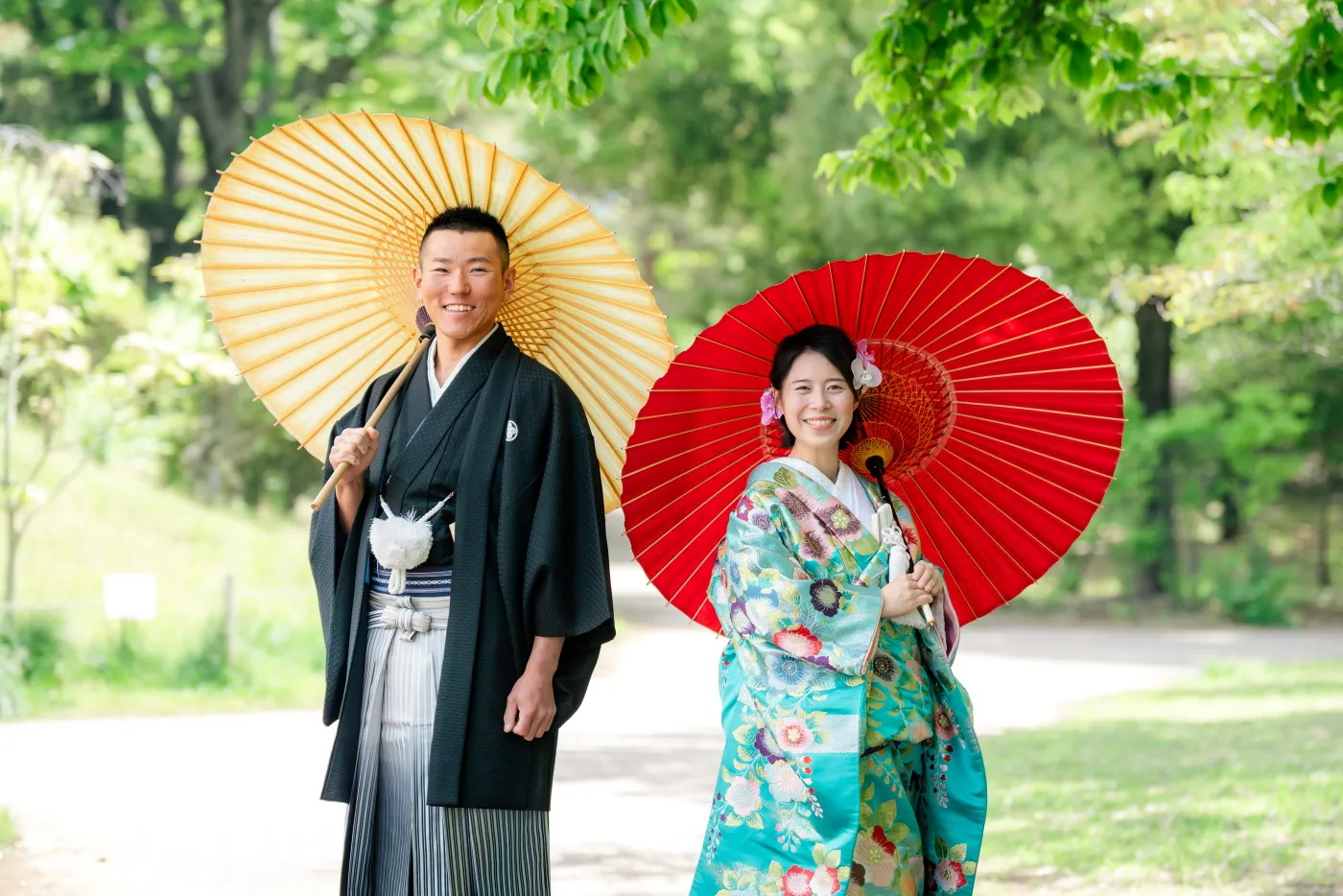 黄色と赤の和傘をさして並ぶ、水色の色打掛の花嫁と黒紋付袴の花婿