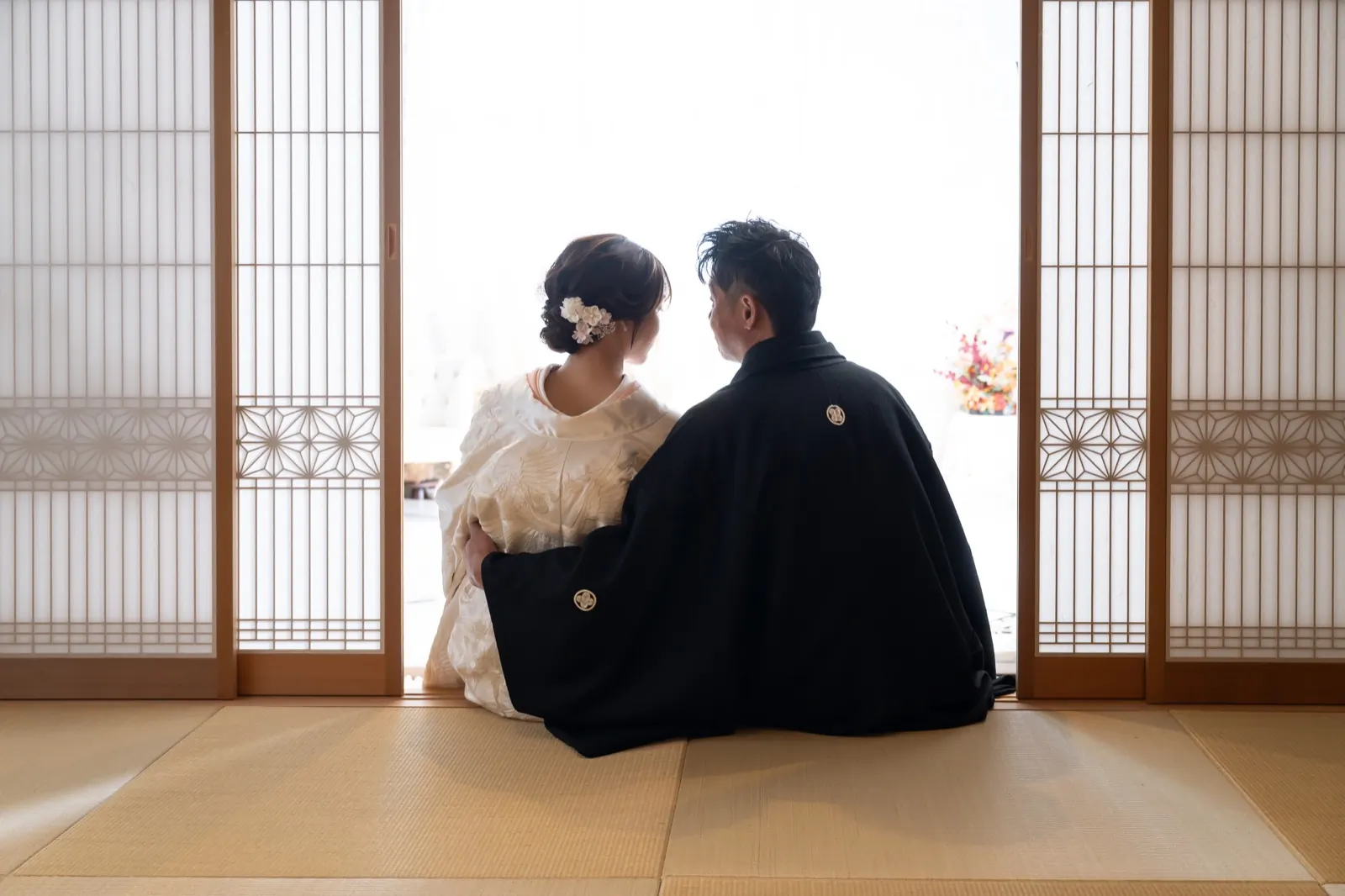 畳の和室で向かい合って座る、白無垢の花嫁と黒紋付袴の花婿