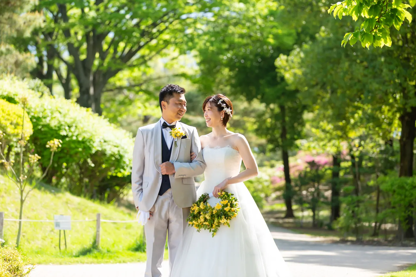 新緑の並木道を歩く、ウェディングドレスの花嫁とタキシードの花婿