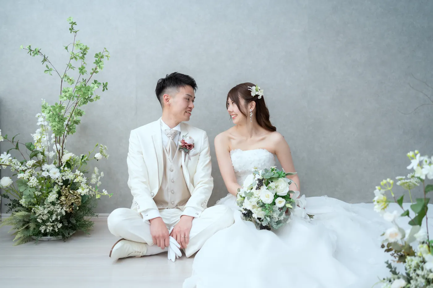装花を配したスタジオで撮影した、ウェディングドレスの花嫁と白いタキシードの花婿