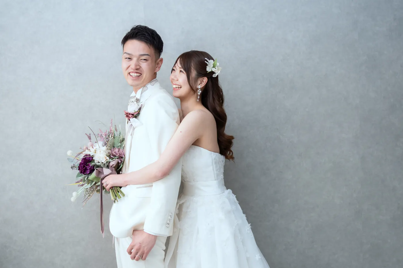 背中合わせに立つ、ウェディングドレスの花嫁と白いタキシードの花婿のスタジオ撮影